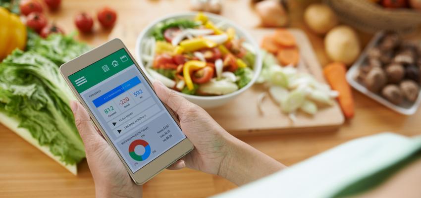 A foto mostra uma pessoa usando um app de auxílio na cozinha enquanto prepara uma refeição saudável.